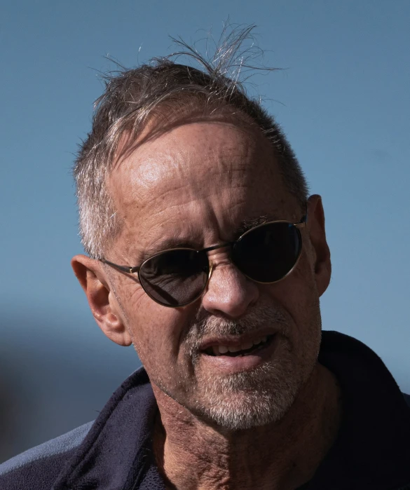 an older man in a jacket, sunglasses, and black shirt