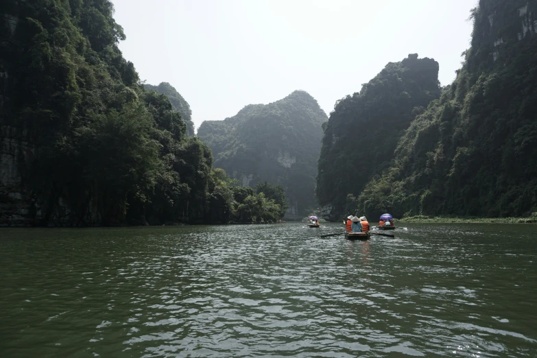 people row boats on the water near several large rocks