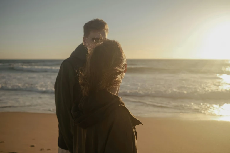 there is a man and a woman standing by the ocean on the sand