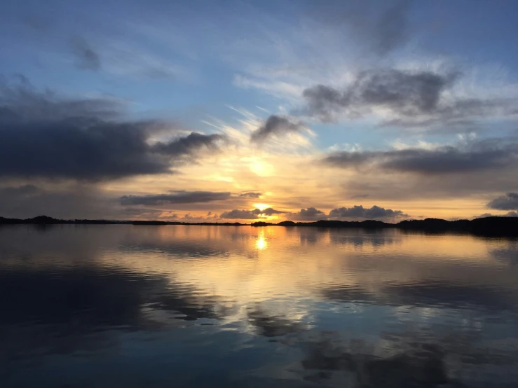 a water body at sunset or sunrise with clouds over it