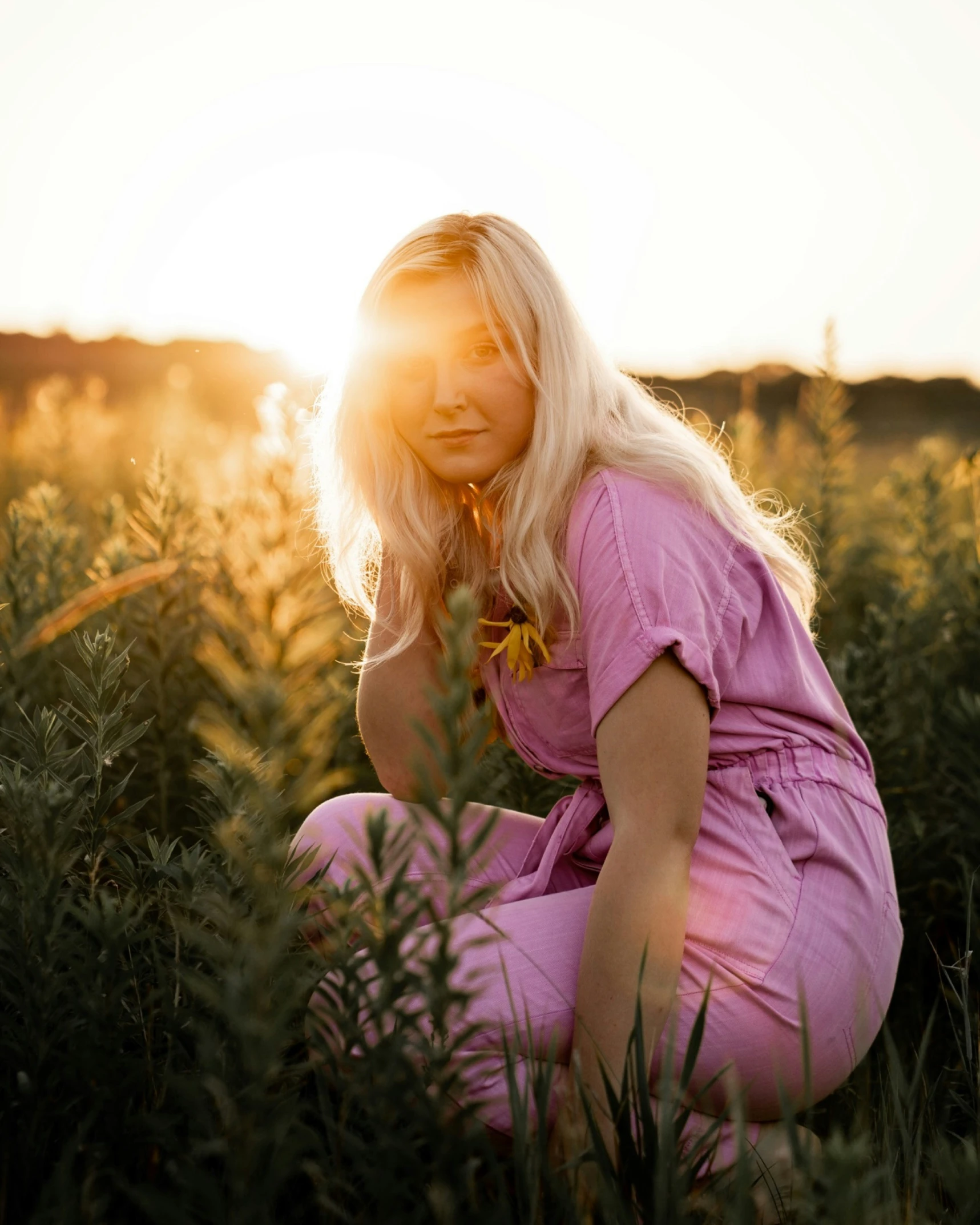 a woman crouches in a field in the sunset