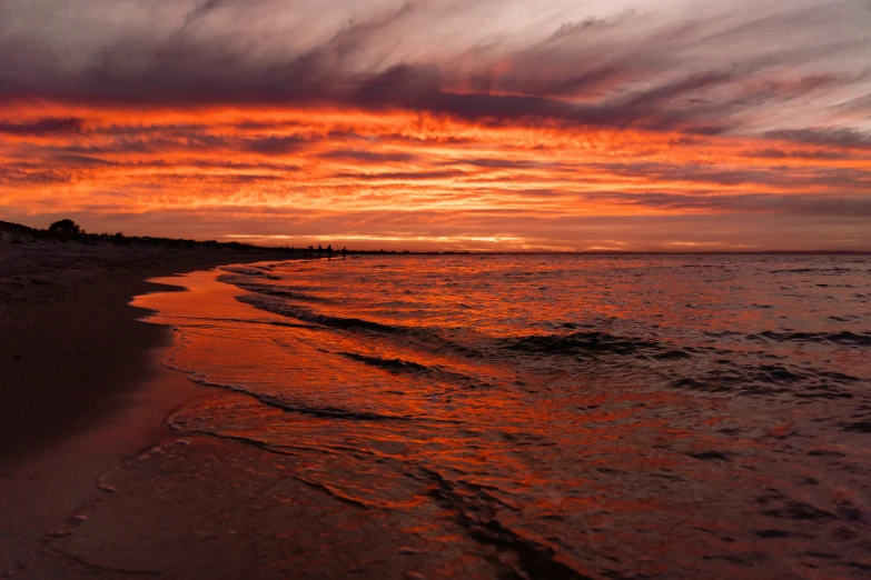 the sun setting on the beach next to a body of water