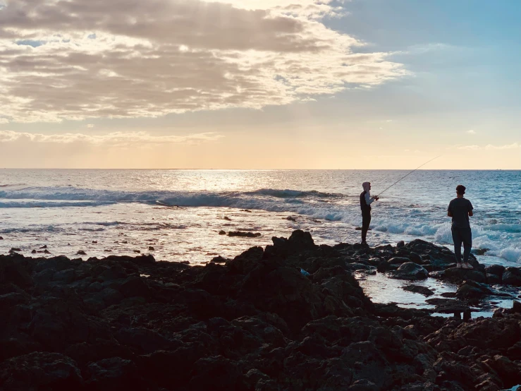 a man standing on rocks holding a fishing rod next to the ocean