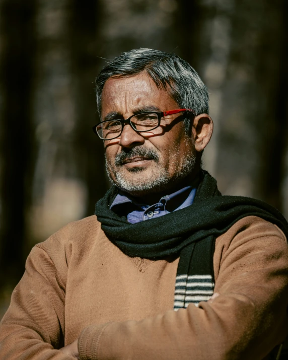 a man with glasses standing in front of some trees