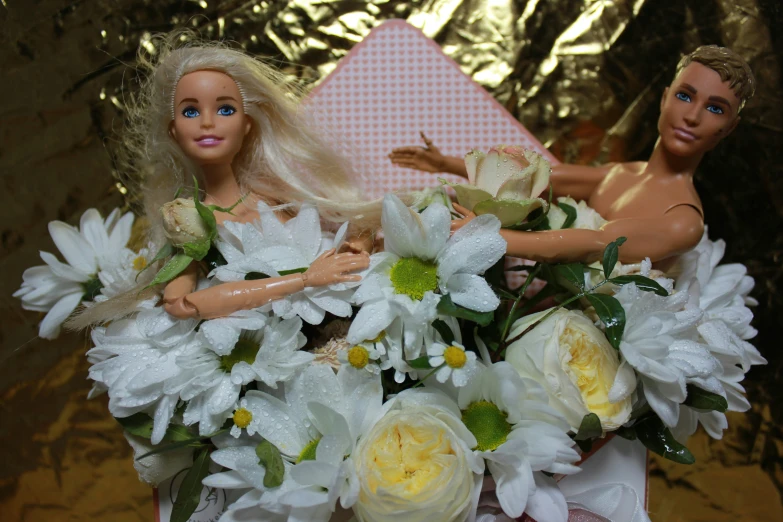 a doll and a blonde barbie sitting in front of a bouquet of flowers