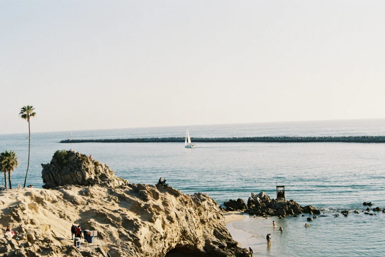 a view from a rock covered beach with some people playing and swimming