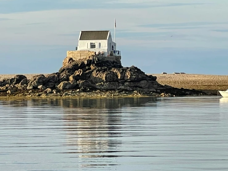 a small house sits on a rocky outcropping by a sailboat