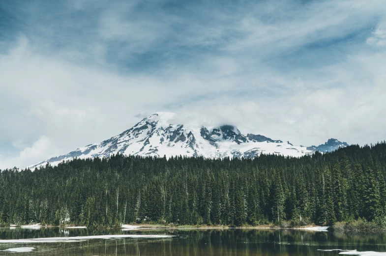 a large snow covered mountain above a lake in front of some trees