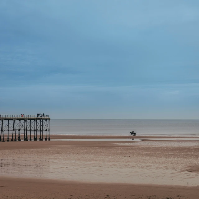 a small group of people walk on the beach by a pier