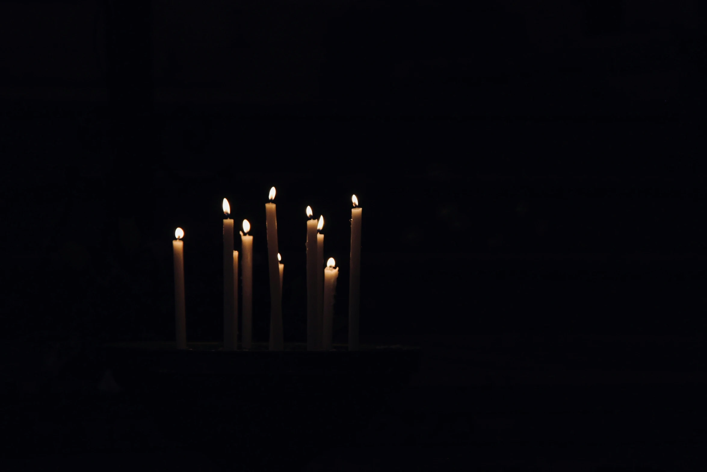 lit candles stand in the darkness with dark background