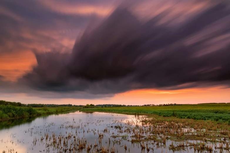 a river runs alongside a field under cloudy skies