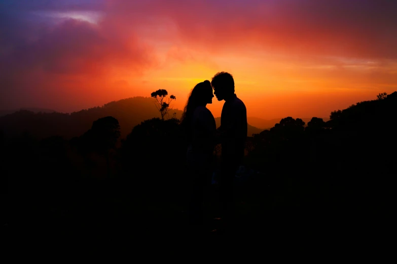 a silhouetted couple kisses while the sun sets