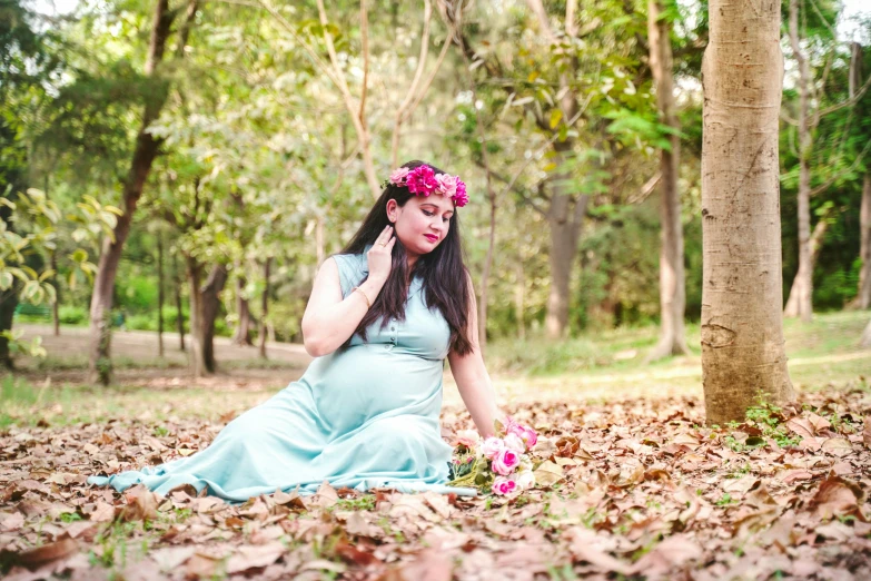 a pregnant woman sitting in leaves talking on a cellphone