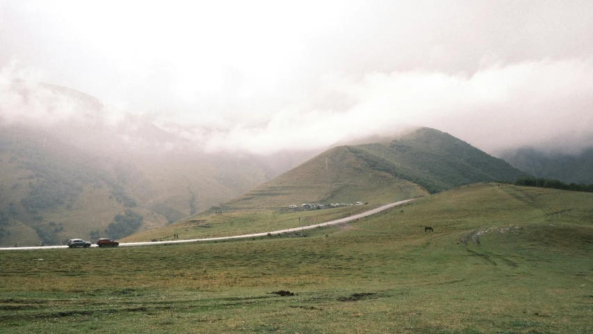 a car driving down a road on a hillside in the fog