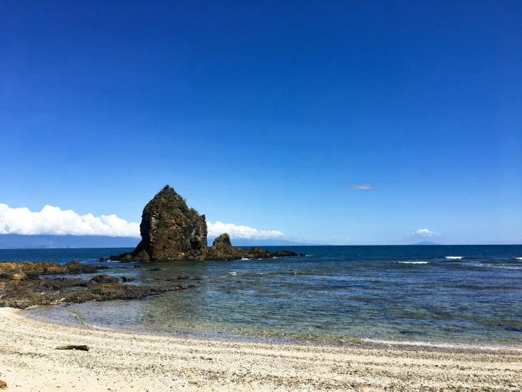 a rock outcropping on a beach near a blue ocean