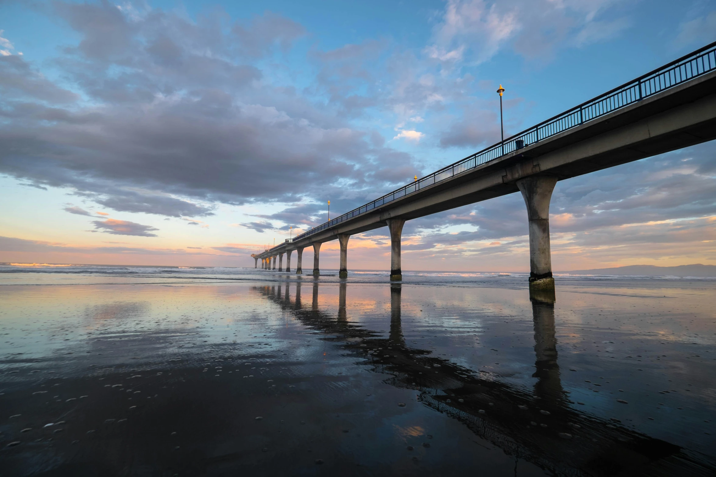 a beach with a wooden bridge and clear water