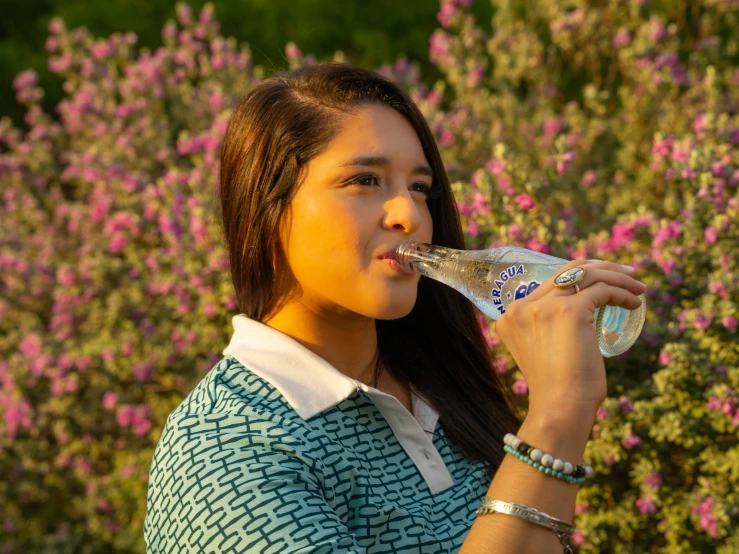 girl drinking from a water bottle in front of pink flowers