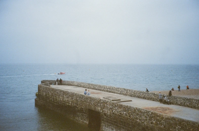 people walk along the wall of a pier on a foggy day