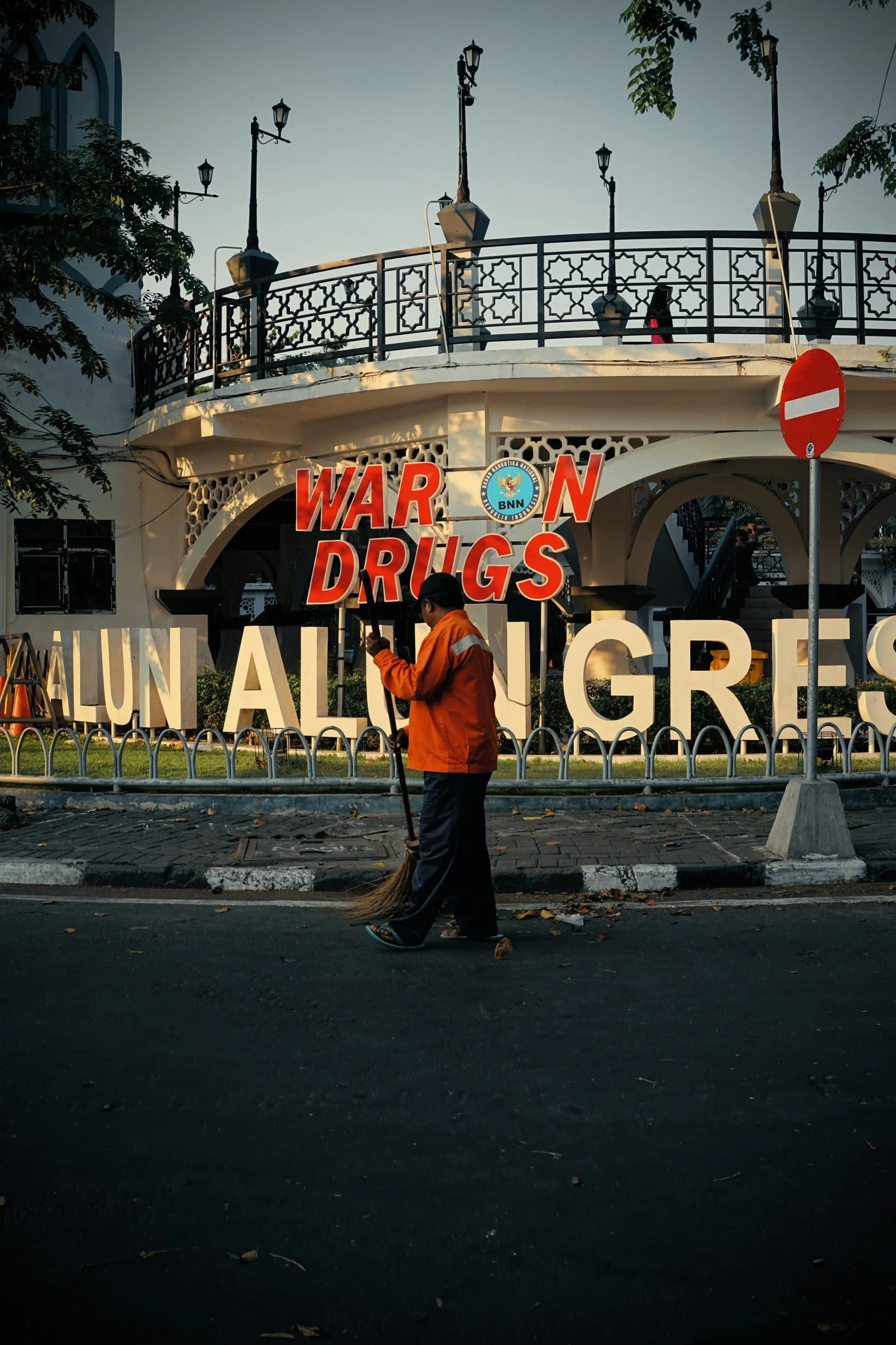 two people walking on the road beside a building with a sign and railing