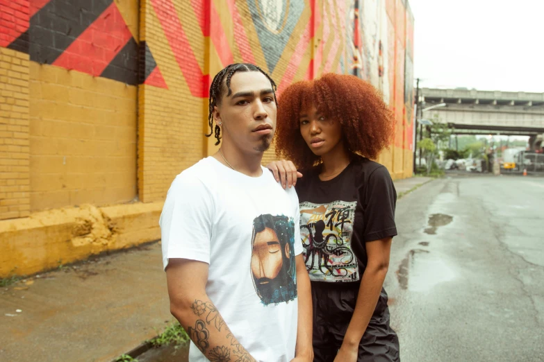 a man with red hair and an afro stands next to a woman with tattoos