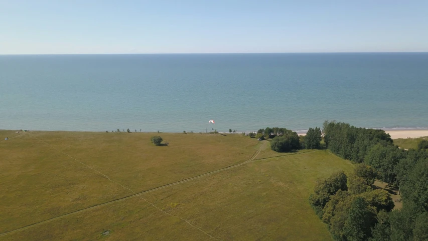 a group of people walking across a lush green field next to the ocean