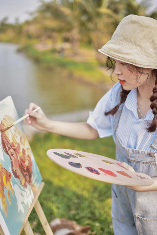 a girl wearing overalls holding a paintbrush painting a picture