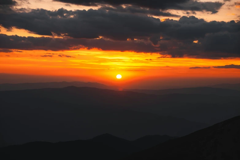 a bright sunset behind the mountains on a cloudy day