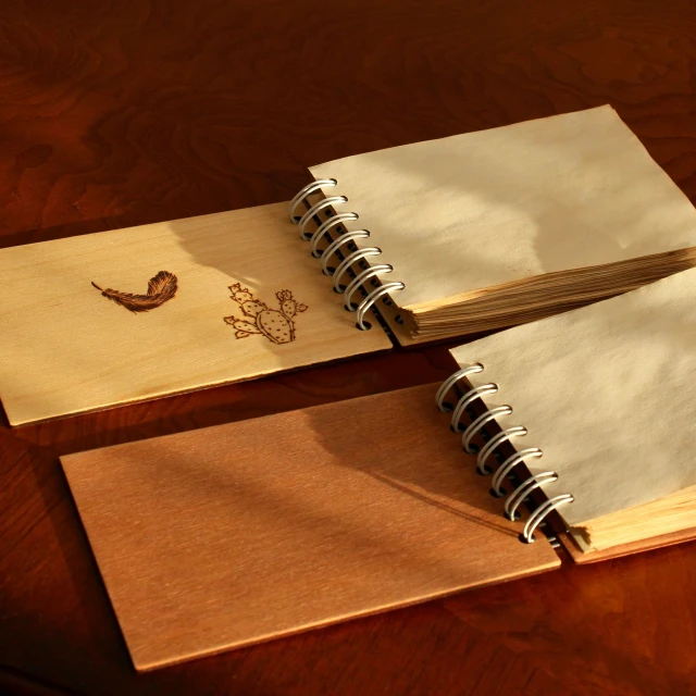 two open notebooks and a sketch book sitting on a wooden desk