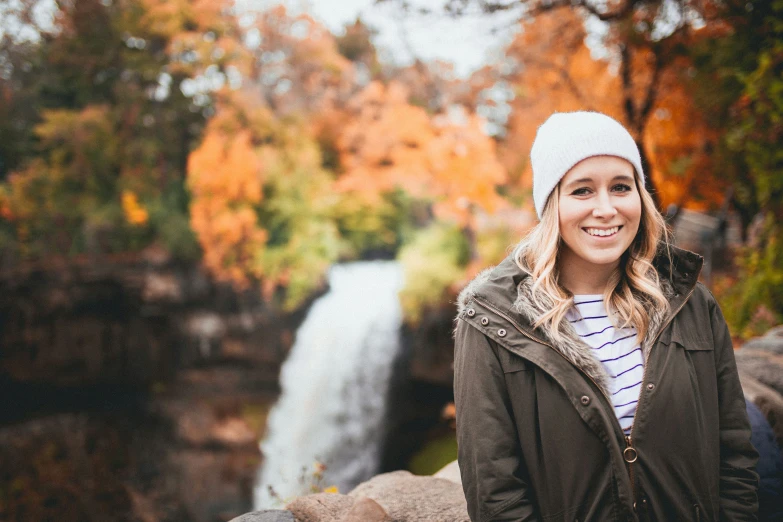 a girl in a hat is standing by a waterfall