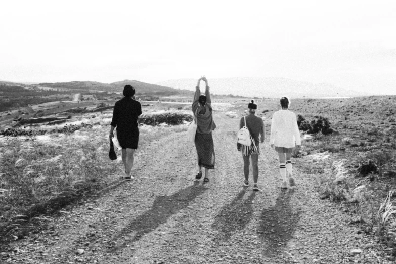 three people standing on a dirt road holding up the same kite