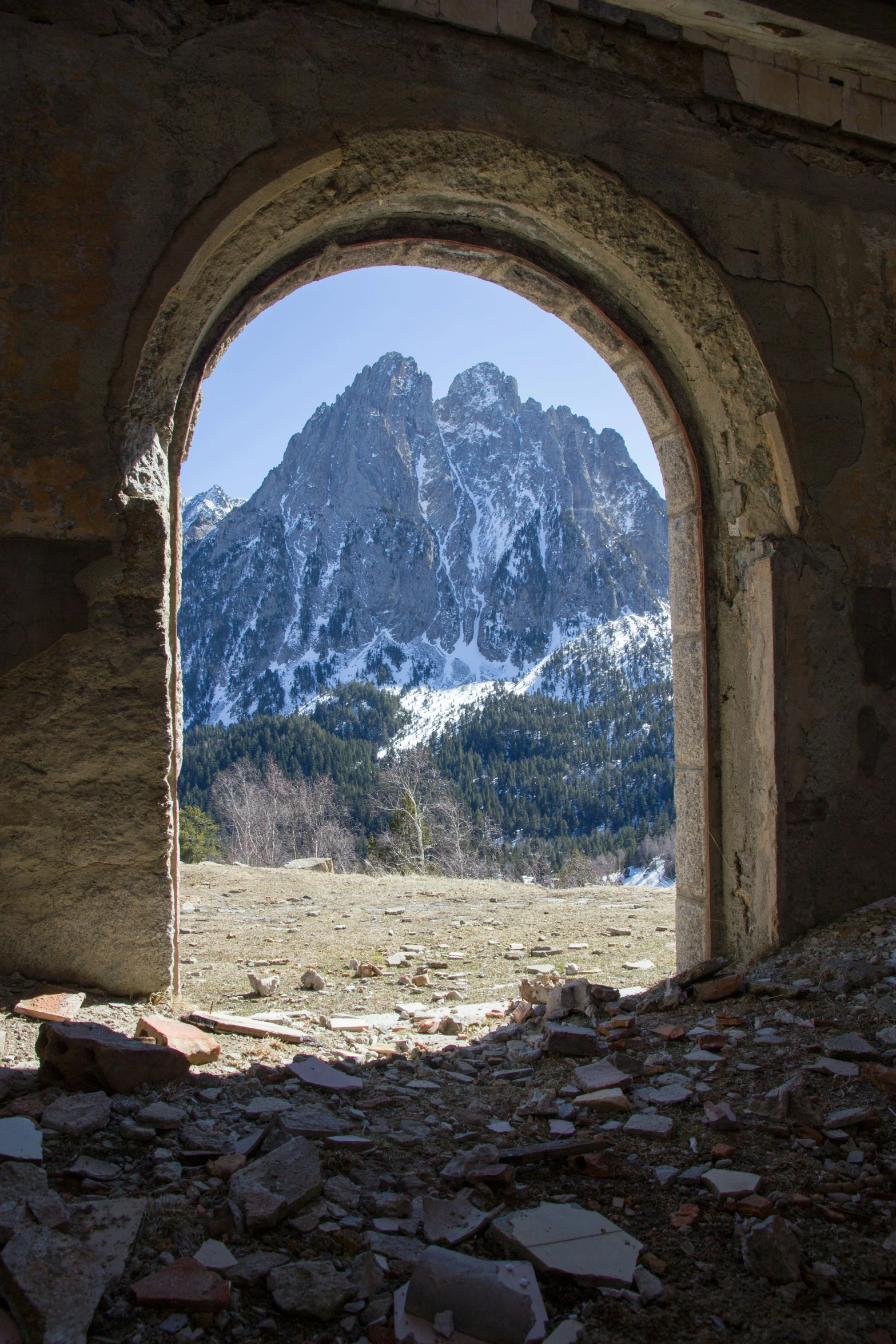 an arched window in an old building with snow covered mountains in the distance