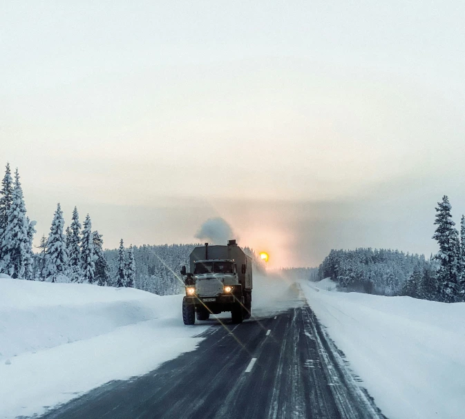 two large vehicles driving on the road covered with snow