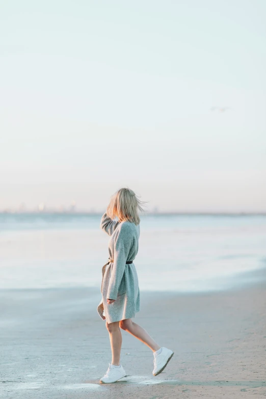 the girl in a light blue coat walks along the beach