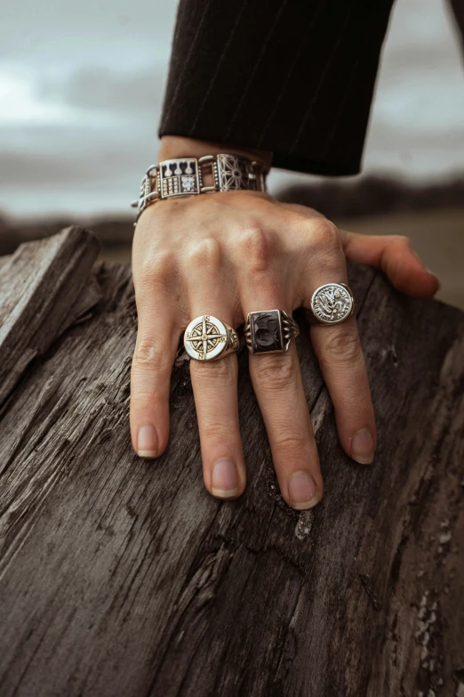 someone is sitting on top of a wood with five rings around their fingers