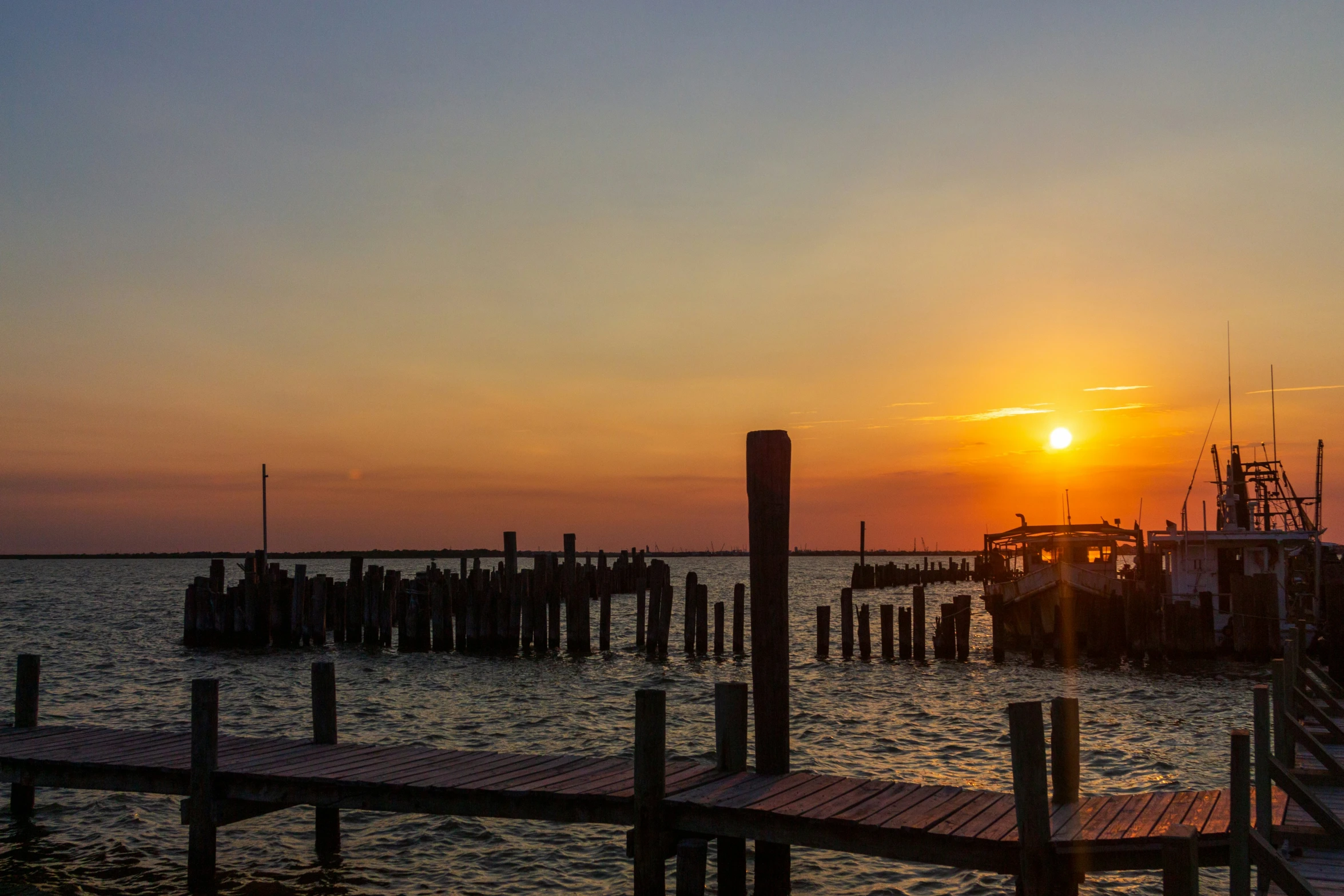 a sunset is seen near the dock at an ocean