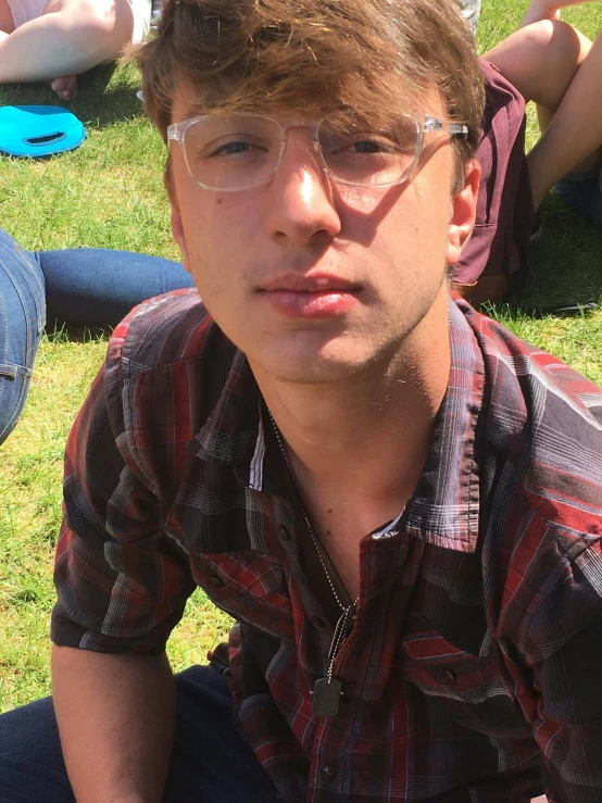 a boy wearing glasses sitting outside in front of people