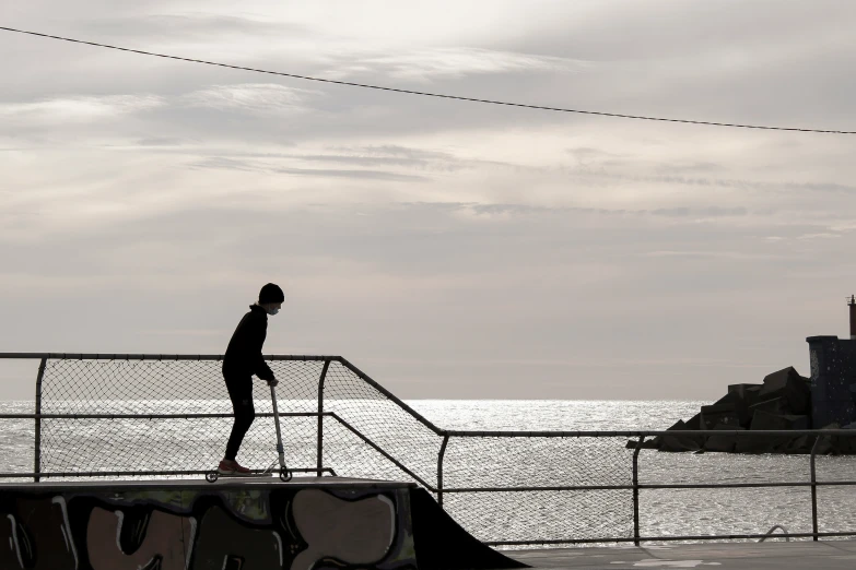 a person walks across a rail near a railing with the sea and buildings in the background