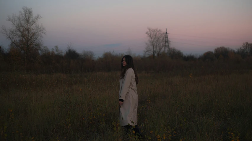 a woman standing in an open field at sunset