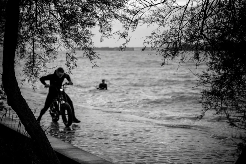 a black and white image of someone riding their bike near the water