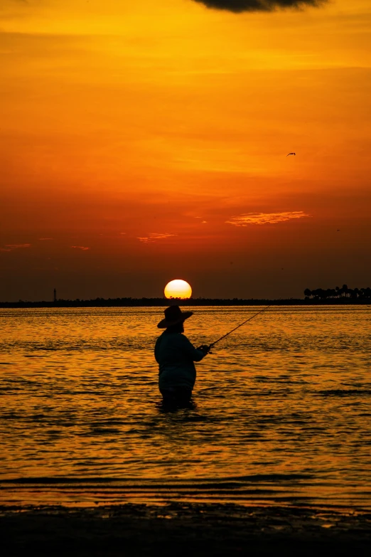 an image of a person wading in the water at sunset