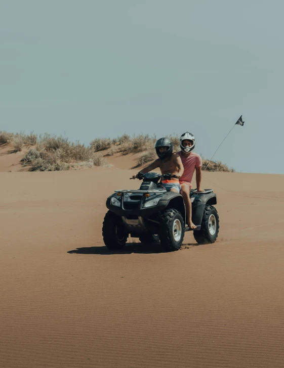 two men riding four wheelers through the sand dunes