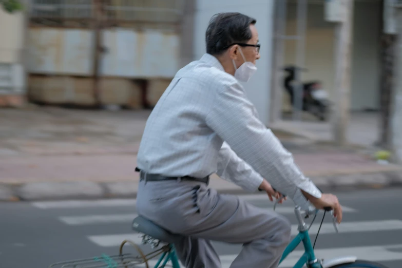 an older man with a surgical mask riding a blue bike