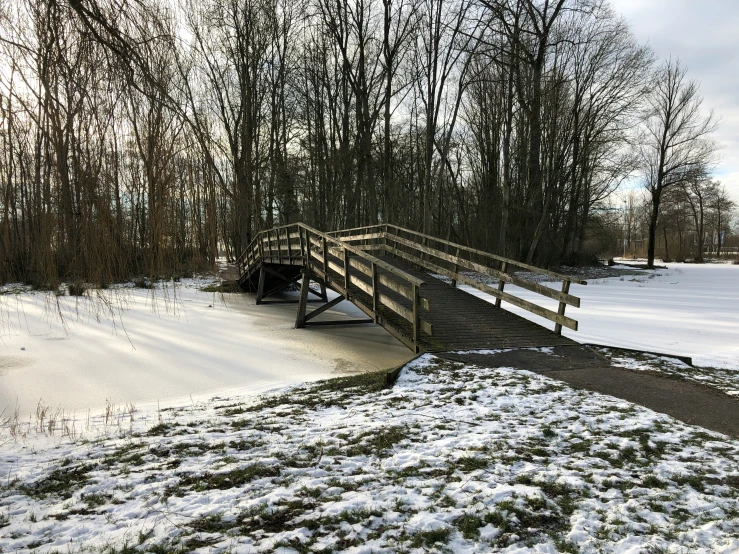 an old wooden bridge over a small stream in the winter snow