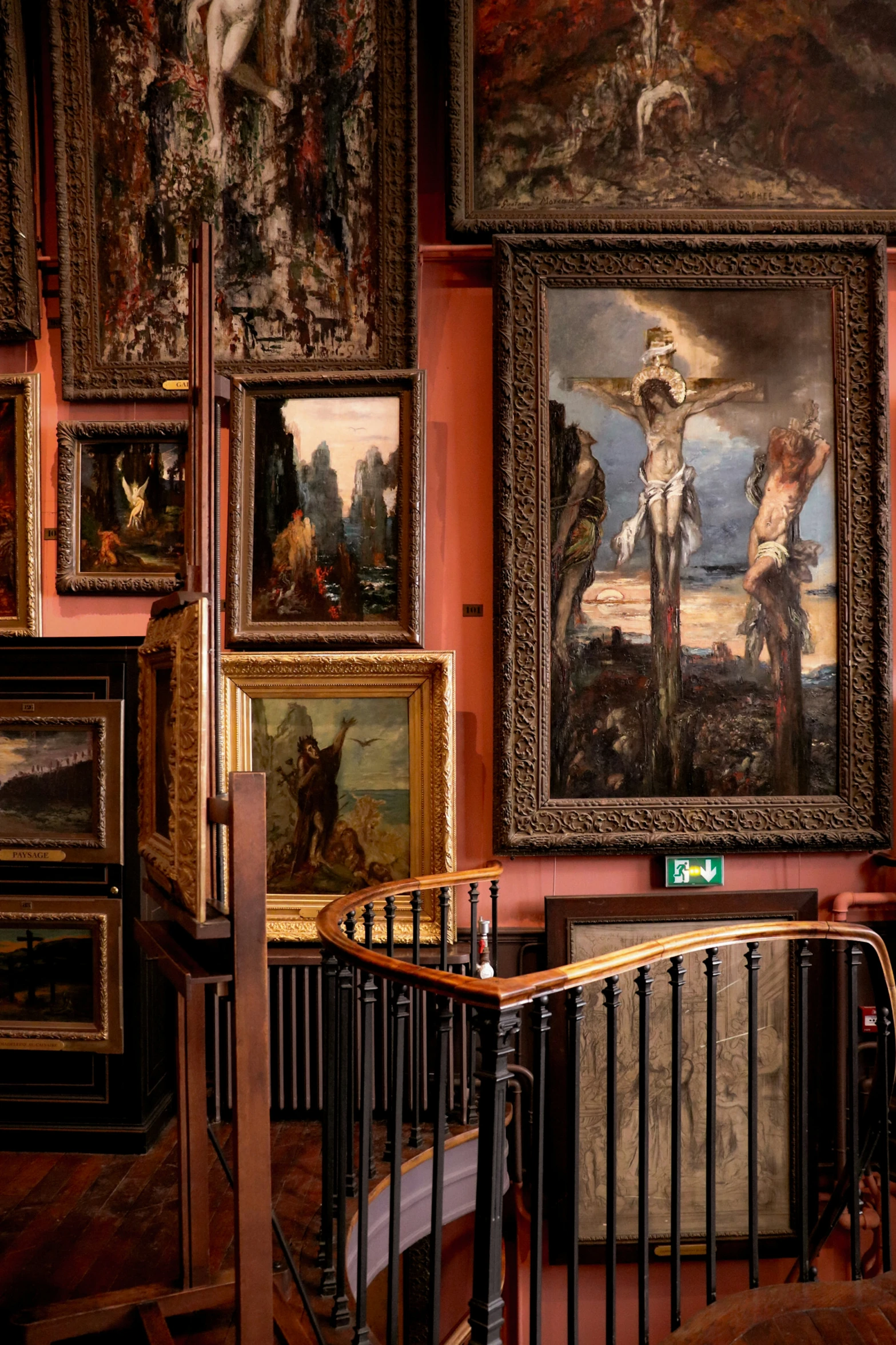 several paintings hung in ornate frames next to a spiral staircase