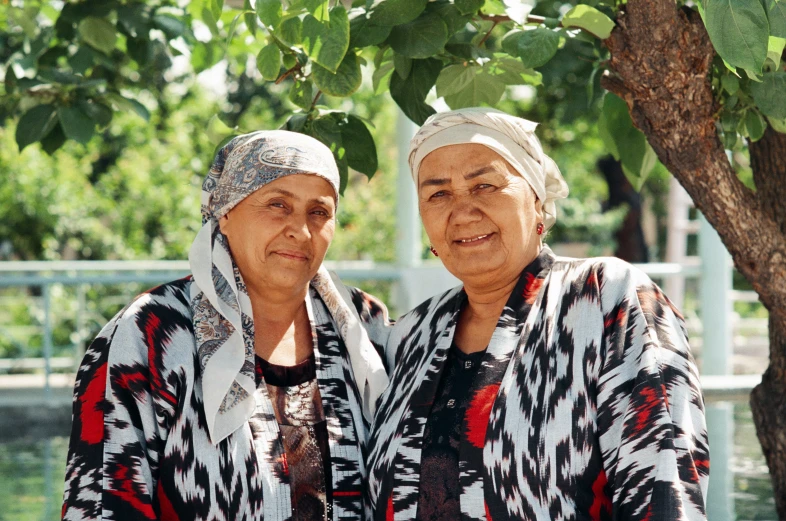 two women are smiling under the tree while standing