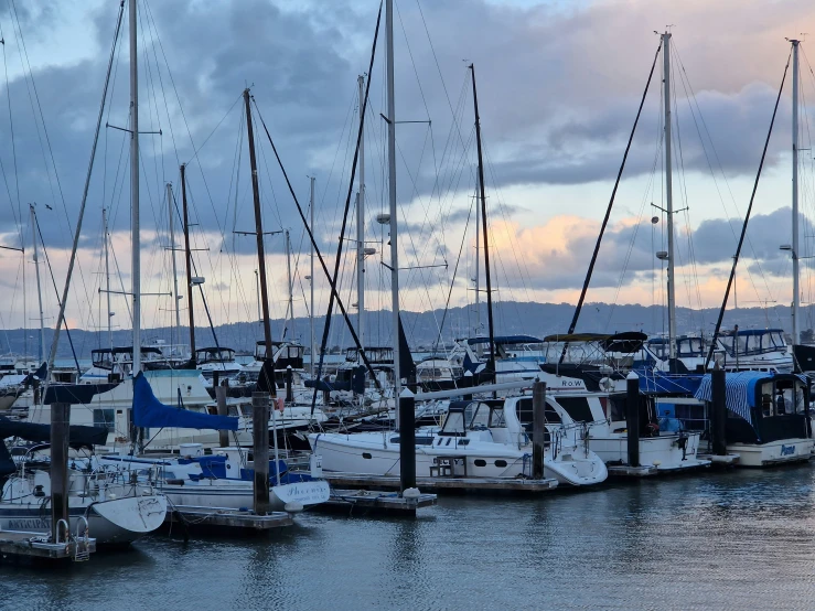 sailboats in the harbor during sunset on a cloudy day