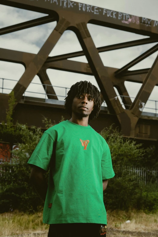 a man in a green shirt standing near a bridge