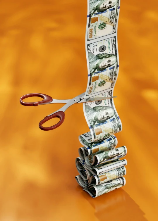 a stack of money, scissors and a bundle of dollars sitting in front of a bright orange backdrop
