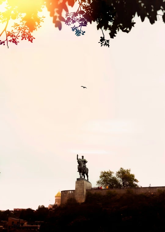 a bird flies near a statue in front of the sun