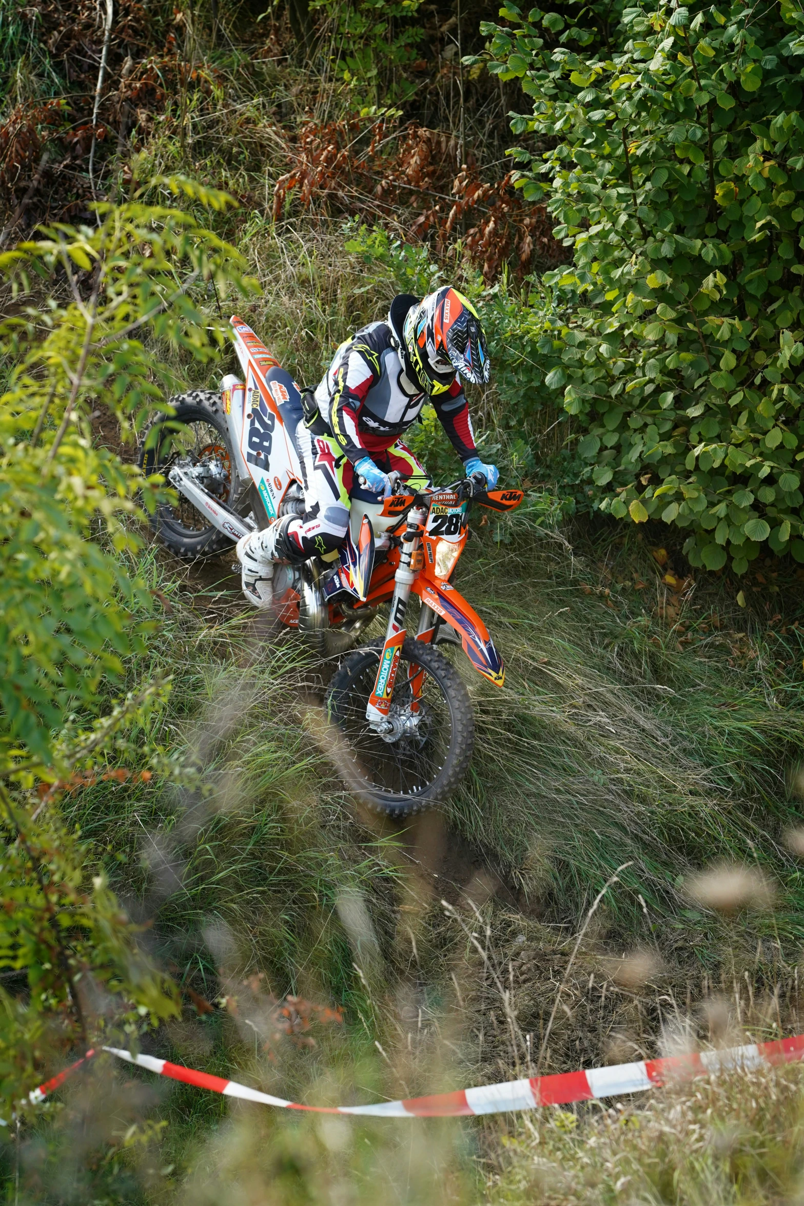 two people on motorcycles in the grass with trees behind them